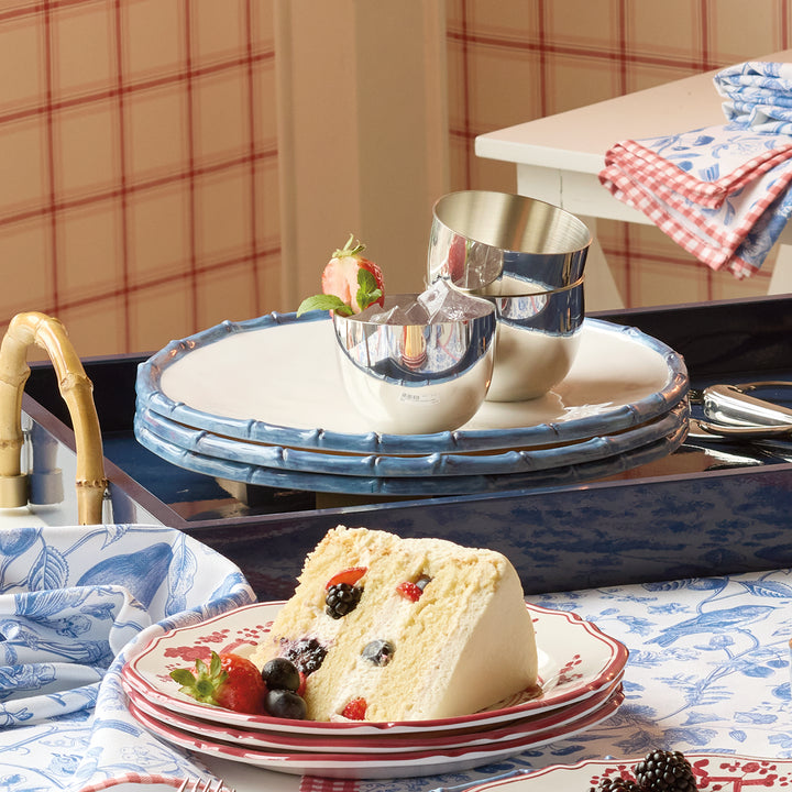 Slice of cake with berries on a melamine dinner plate, placed on a table with plaid tablecloth and background.